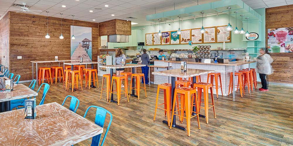 Inside of a tropical smoothie with orange chairs and a counter top or order.