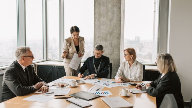 5 adults sitting around a table with paper and applications discussing business matters